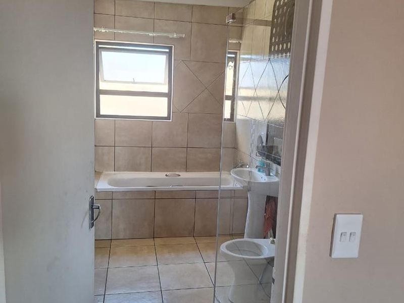 A functional bathroom featuring a bathtub, pedestal basin, toilet, and a glass-enclosed shower with neutral wall and floor tiling.