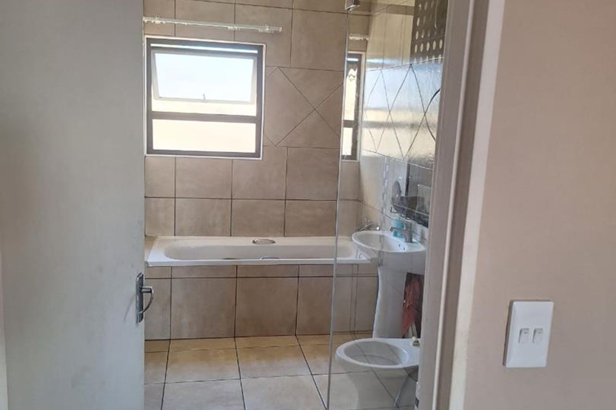 A functional bathroom featuring a bathtub, pedestal basin, toilet, and a glass-enclosed shower with neutral wall and floor tiling.