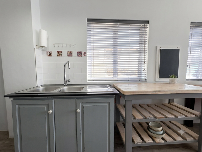 A functional kitchen area featuring a double bowl stainless steel sink, subway tile splashback, and timber-topped cabinetry with grey painted finish.