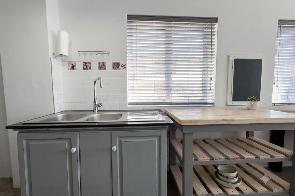 A functional kitchen area featuring a double bowl stainless steel sink, subway tile splashback, and timber-topped cabinetry with grey painted finish.