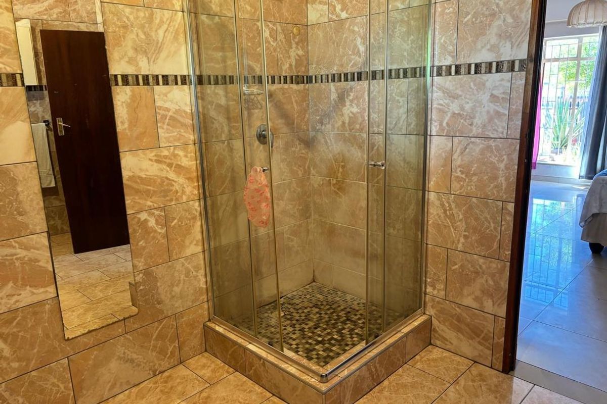 A bathroom featuring a corner glass shower enclosure with mosaic floor tiling and full-height marble-effect wall tiles.