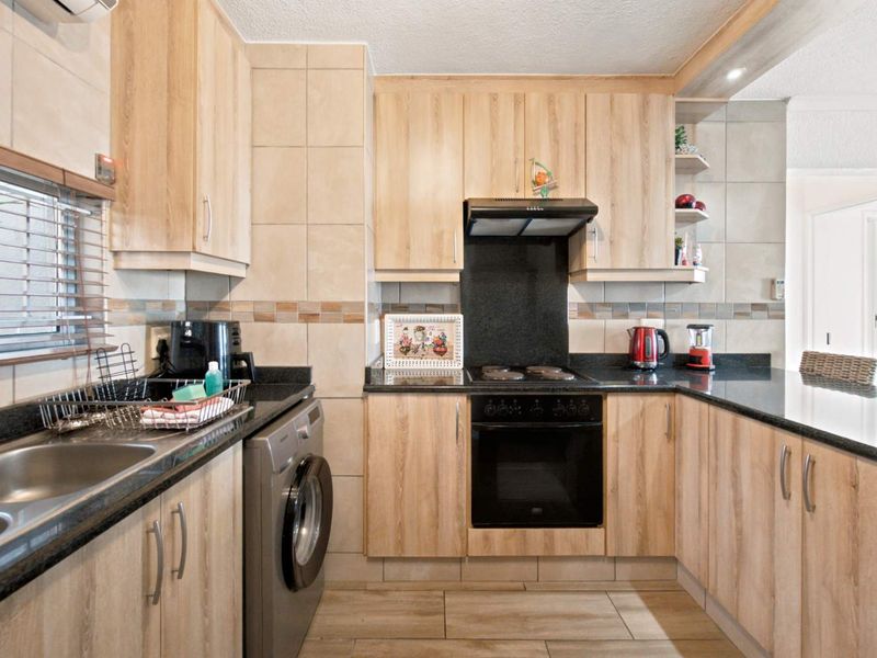 A functional kitchen featuring light wood-finish cabinetry, dark granite countertops, built-in oven, electric hob, and integrated laundry plumbing.