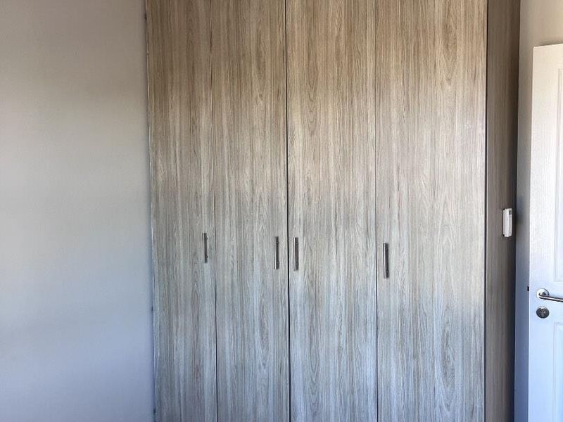 A clean bedroom featuring a modern wood-finish built-in wardrobe, tiled flooring, and decorative crown molding.