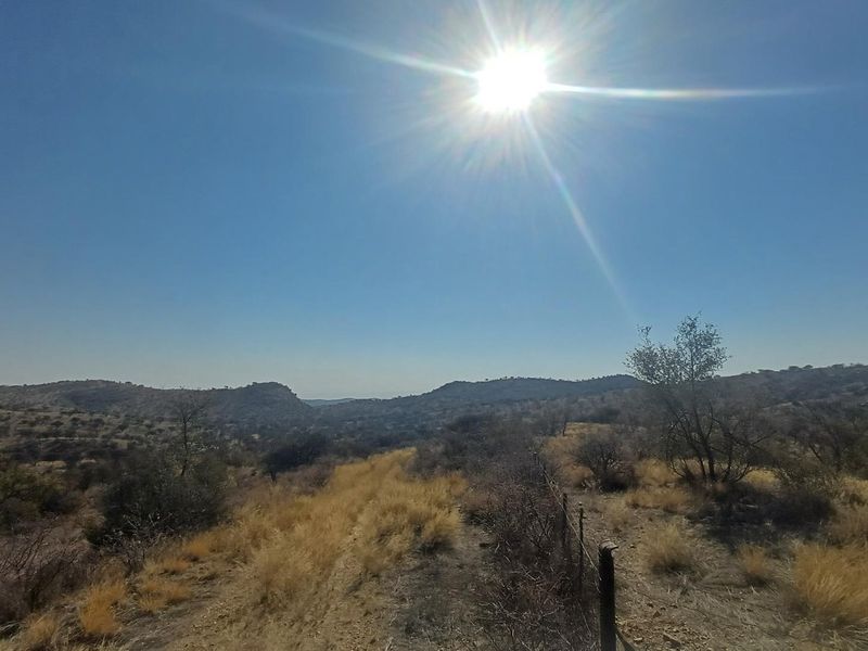 Expansive landscape view of the farm property featuring rolling hills and natural vegetation under a bright sun.