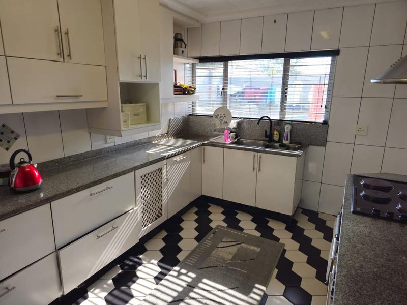 A functional kitchen featuring granite countertops, white cabinetry, a double basin sink, and a built-in hob with an extractor fan.