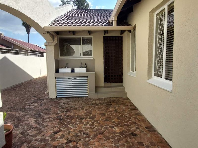 A well-maintained rear courtyard featuring paved flooring, a covered outdoor wash area with dual basins, and secure access points to the main dwelling.
