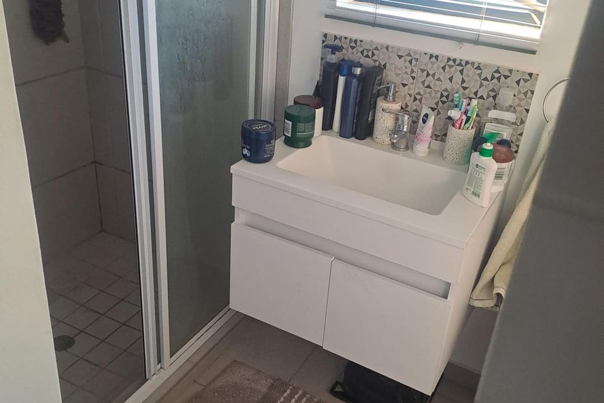 A functional bathroom featuring a modern wall-mounted vanity with basin, a glass-enclosed shower, and decorative tiled splashback.