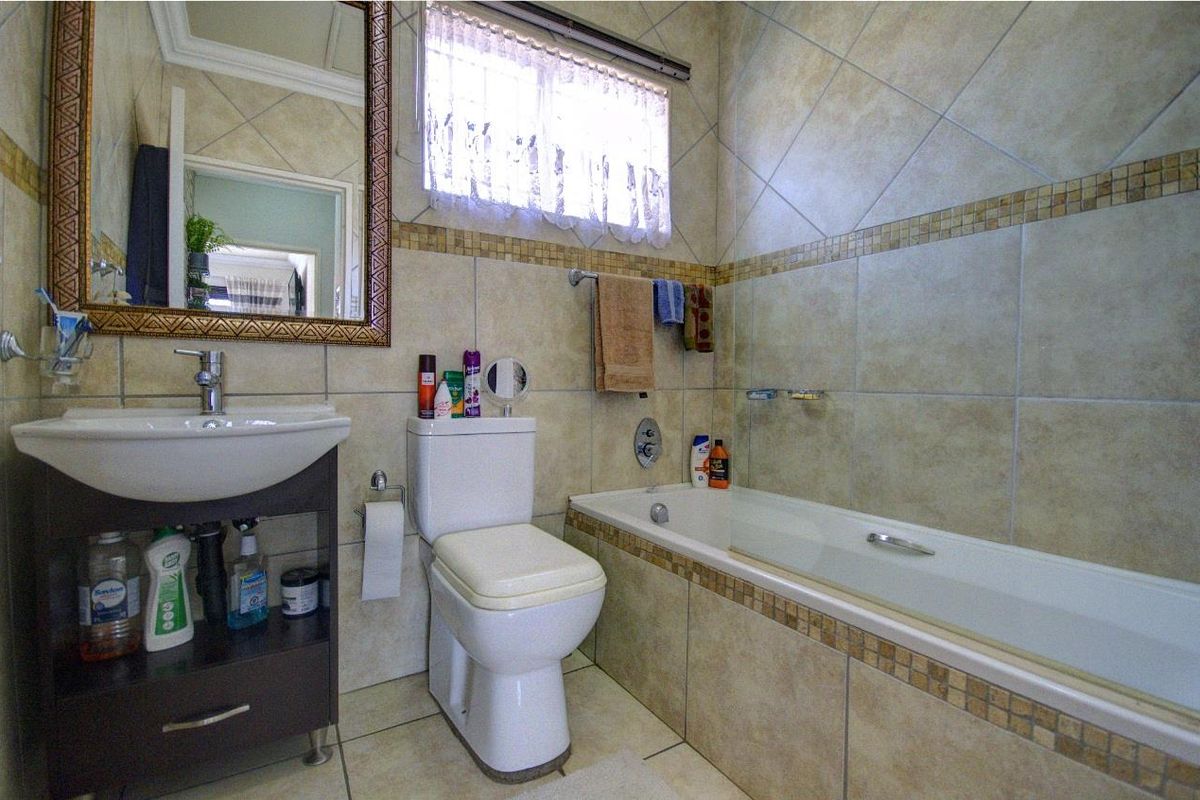 A functional bathroom featuring a built-in bathtub, pedestal vanity with basin, and tiled walls with decorative mosaic accents.