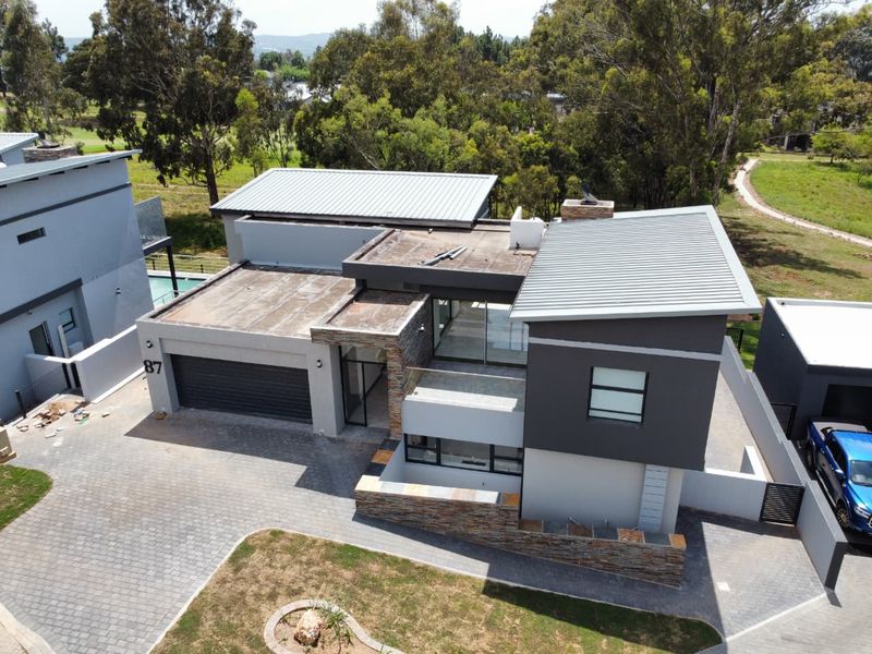 Aerial view of a modern multi-level house featuring a combination of metal roofing, stone cladding, and a paved driveway with a double garage.