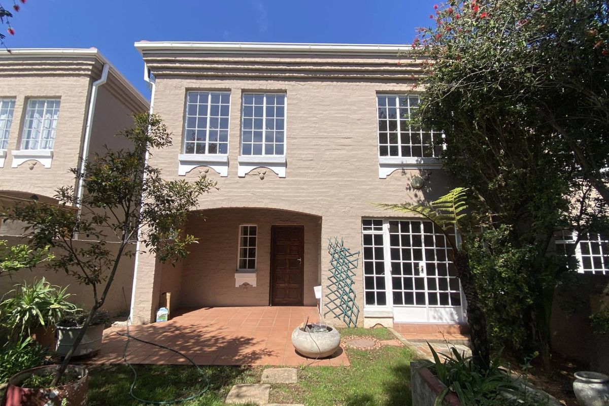 Rear view of the townhouse featuring a covered patio, tiled flooring, and classic grid-pattern windows set against a painted brick facade.
