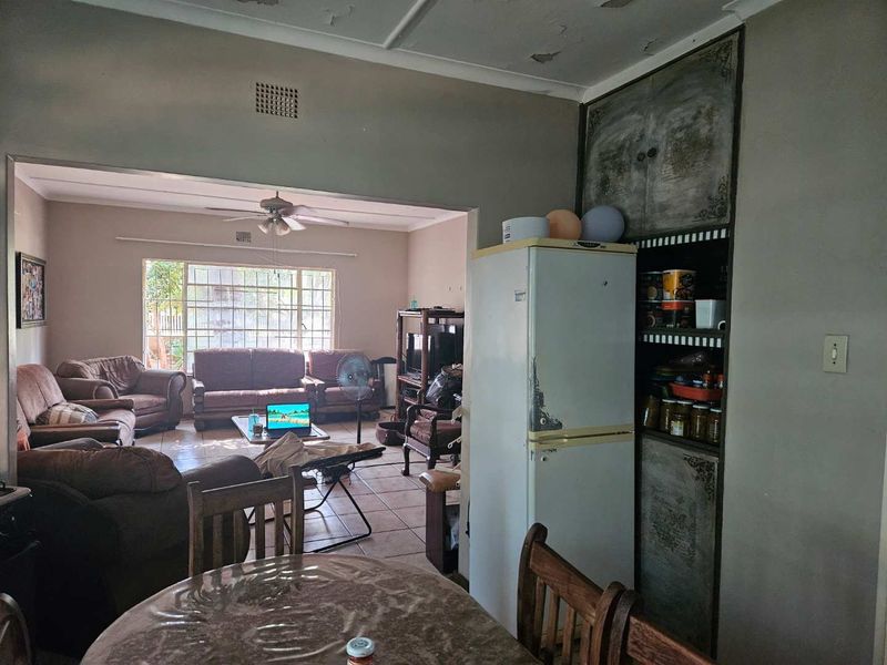 Open plan living and dining area featuring tiled floors, a ceiling fan, and built-in storage cabinetry, with visible signs of wear on the ceiling.