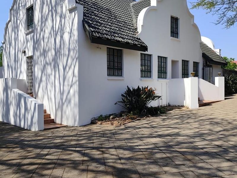 A well-maintained Cape Dutch style house featuring a distinctive gabled facade, tiled roof, and a spacious paved driveway.