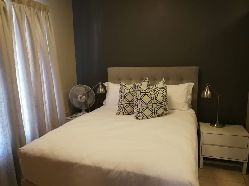 A cozy bedroom featuring a neutral color palette, an accent wall, and tiled flooring, providing a comfortable and functional sleeping space.