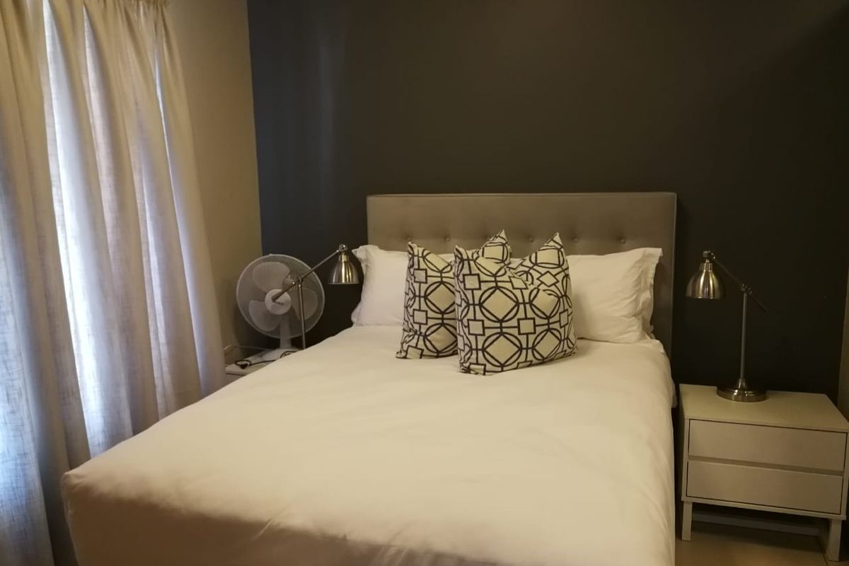 A cozy bedroom featuring a neutral color palette, an accent wall, and tiled flooring, providing a comfortable and functional sleeping space.