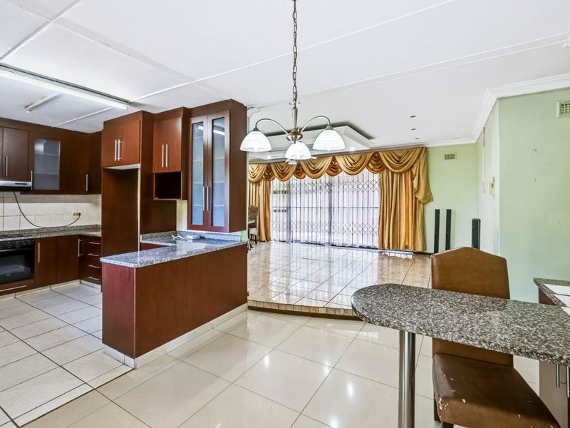Open plan kitchen and living area featuring dark wood cabinetry, granite countertops, tiled flooring, and a raised living space with large sliding doors.