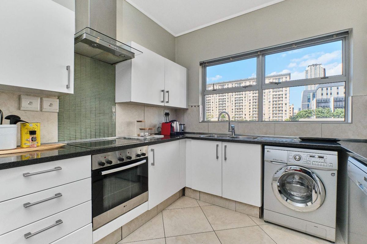 Modern kitchen featuring white cabinetry, granite countertops, integrated oven, extractor fan, and a built-in washing machine with a city view.