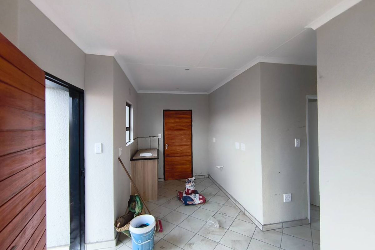 An empty interior space featuring tiled flooring, neutral wall finishes, and a small built-in counter area with a wooden door.