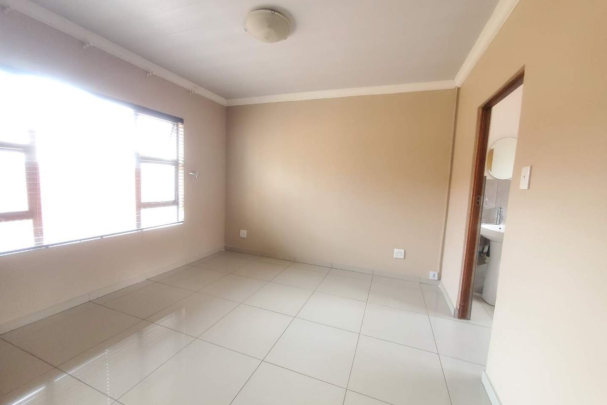 A bright, empty bedroom featuring neutral wall paint, tiled flooring, and an adjoining en-suite bathroom.