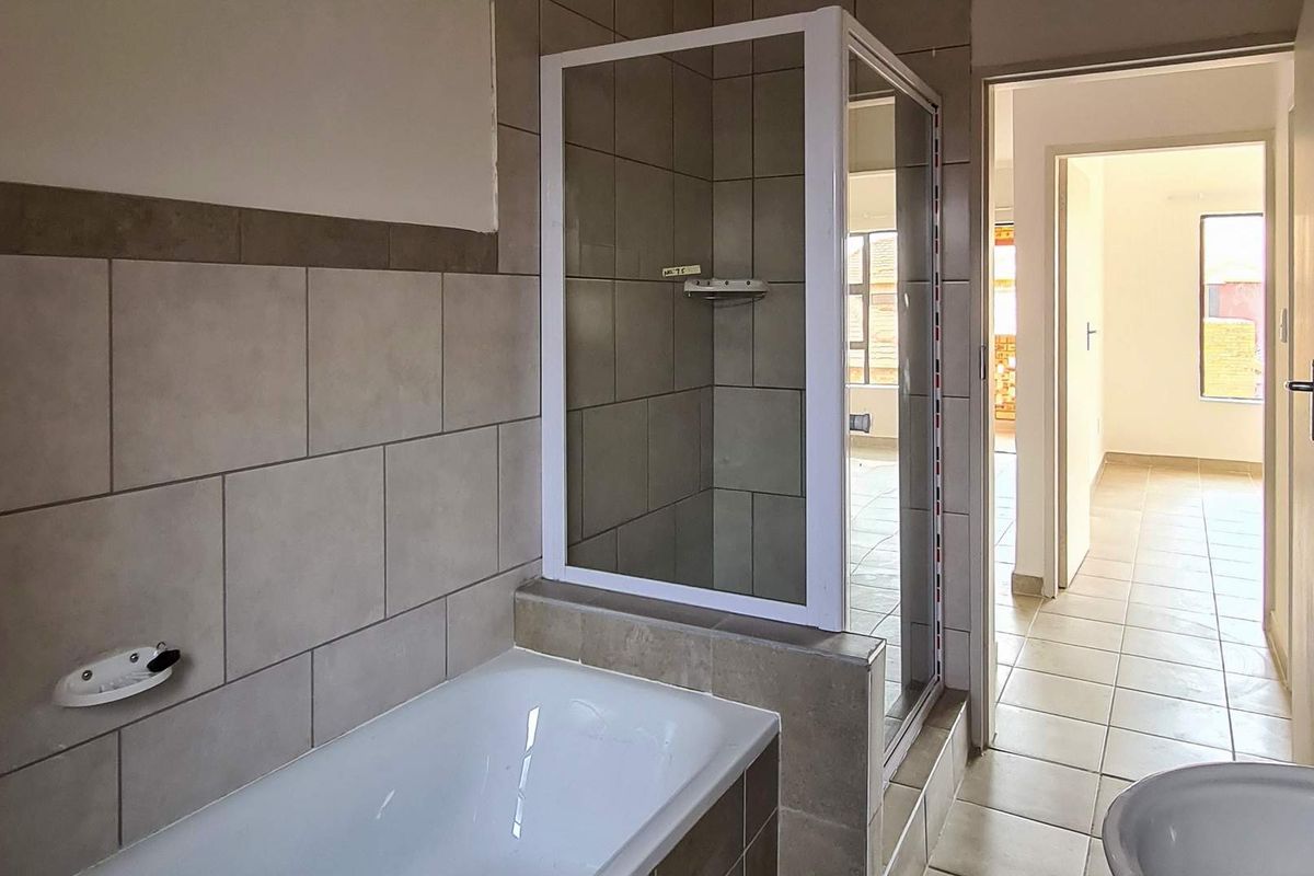 A functional bathroom featuring a bathtub, separate shower enclosure, and neutral wall and floor tiling, presented in a clean, vacant condition.