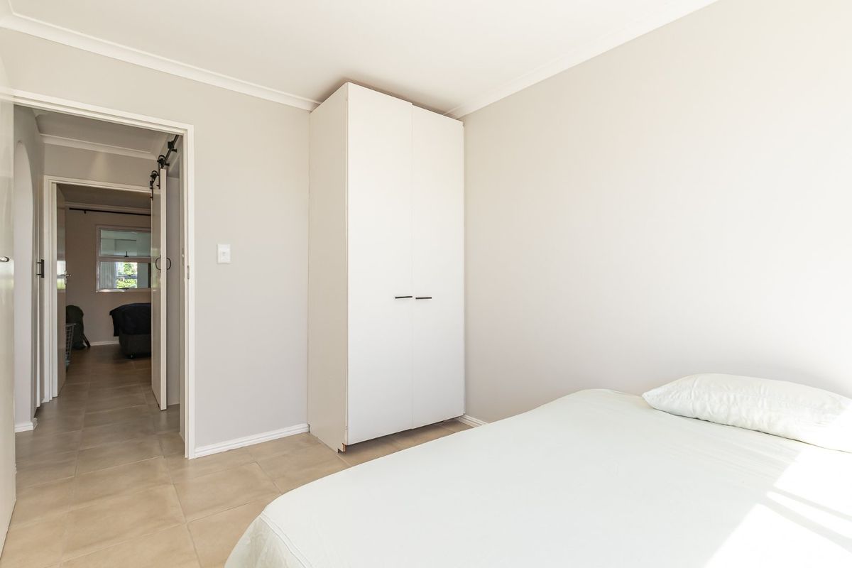 A bright bedroom featuring neutral walls, tiled flooring, and a built-in wardrobe, with a view into the adjacent hallway.