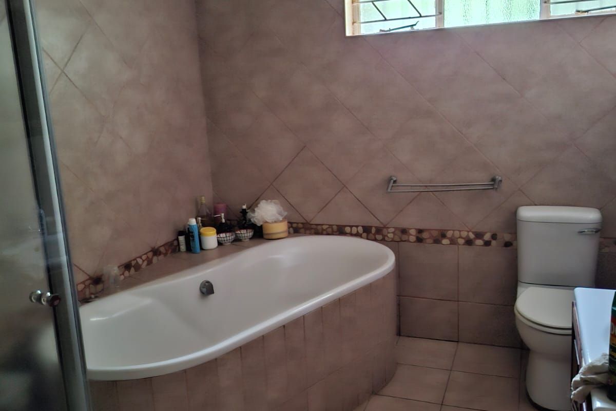 A functional bathroom featuring a built-in bathtub, separate shower enclosure, toilet, and vanity with tiled finishes throughout.