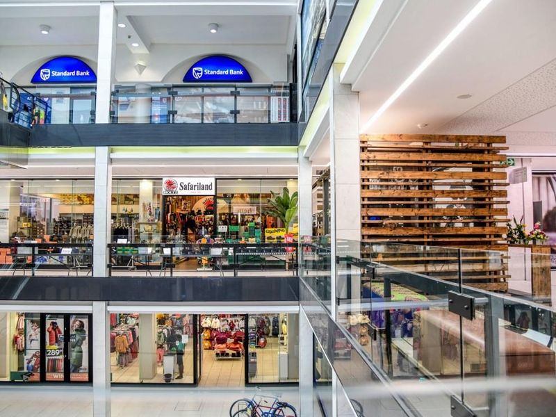 A multi-level retail shopping center atrium featuring glass balustrades, modern lighting, and various storefronts across multiple floors.