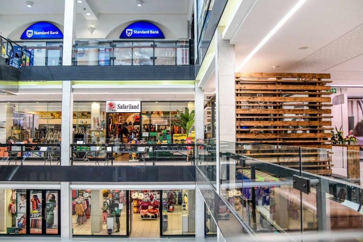 A multi-level retail shopping center atrium featuring glass balustrades, modern lighting, and various storefronts across multiple floors.
