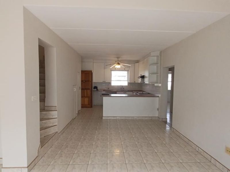 An open-plan living and kitchen area featuring tiled flooring, a functional kitchen peninsula with built-in cabinetry, and an integrated staircase.