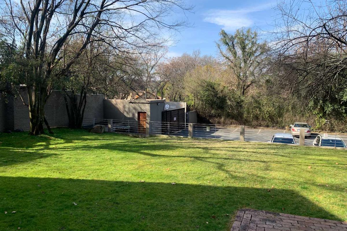 A view of the rear exterior featuring a well-maintained lawn, perimeter wall with security fencing, and an adjacent paved parking area.