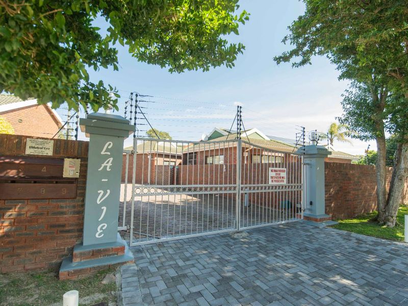 Front entrance view of the townhouse complex featuring a brick boundary wall, secure metal gate, and electric fencing.