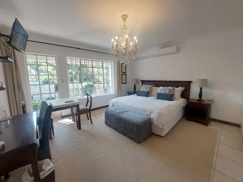 Spacious bedroom featuring a crystal chandelier, split-system air conditioning, and large windows providing natural light and garden views.