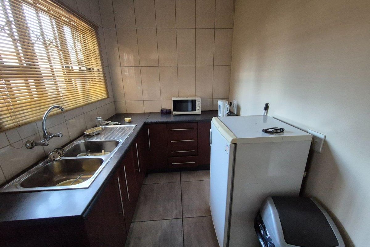 Compact kitchen featuring dark wood cabinetry, dark laminate countertops, double stainless steel sink, and tiled splashbacks.