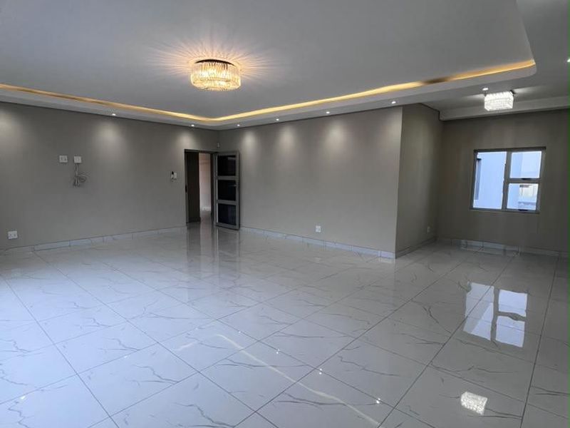 Spacious, modern living area featuring high-gloss marble-look floor tiles, recessed ceiling with ambient LED lighting, and contemporary crystal light fixtures.