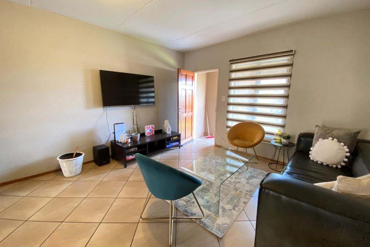 A living room featuring tiled flooring, a window with fitted zebra blinds, and a doorway leading to an adjacent space.