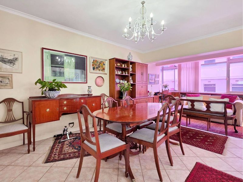 A dining room featuring ceramic floor tiles, a decorative crystal chandelier, and coved cornicing, offering a traditional layout with natural light.