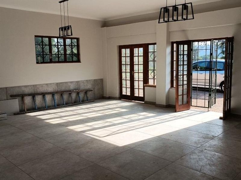 Spacious, light-filled living area featuring large format floor tiles, classic french doors with security gates, and modern pendant lighting.