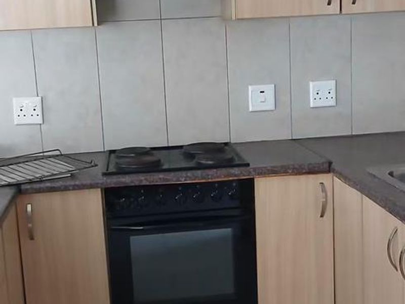 A functional kitchen featuring light wood-finish cabinetry, dark countertops, a built-in oven with hob, extractor fan, and neutral tiled flooring and backsplash.