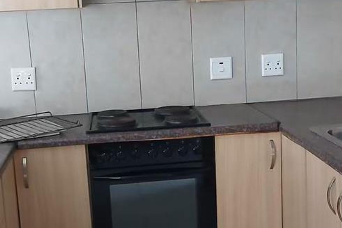 A functional kitchen featuring light wood-finish cabinetry, dark countertops, a built-in oven with hob, extractor fan, and neutral tiled flooring and backsplash.