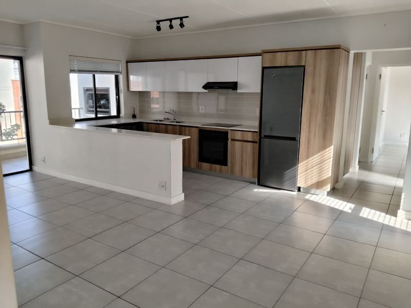 Modern open-plan kitchen featuring sleek cabinetry, integrated appliances, tiled flooring, and a breakfast bar, seamlessly flowing into the living area.