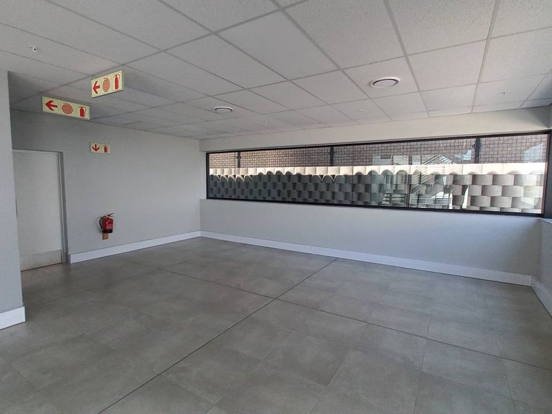 A clean, modern, and empty office space featuring tiled flooring, a suspended ceiling with recessed lighting, and large windows providing natural light.