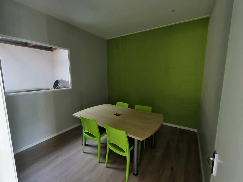 A functional office space featuring laminate flooring, recessed lighting, and an internal window looking into an adjacent area.