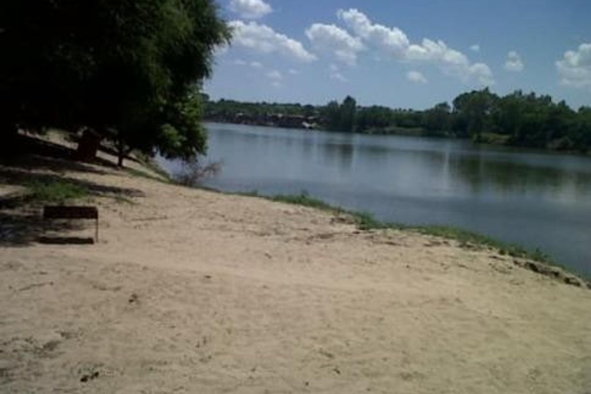 A scenic view of a tranquil riverfront with a sandy beach area and mature trees along the bank.