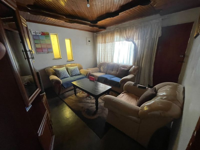 A living room featuring a timber tongue and groove ceiling and vertical slit windows, offering a dated aesthetic ready for modernization.