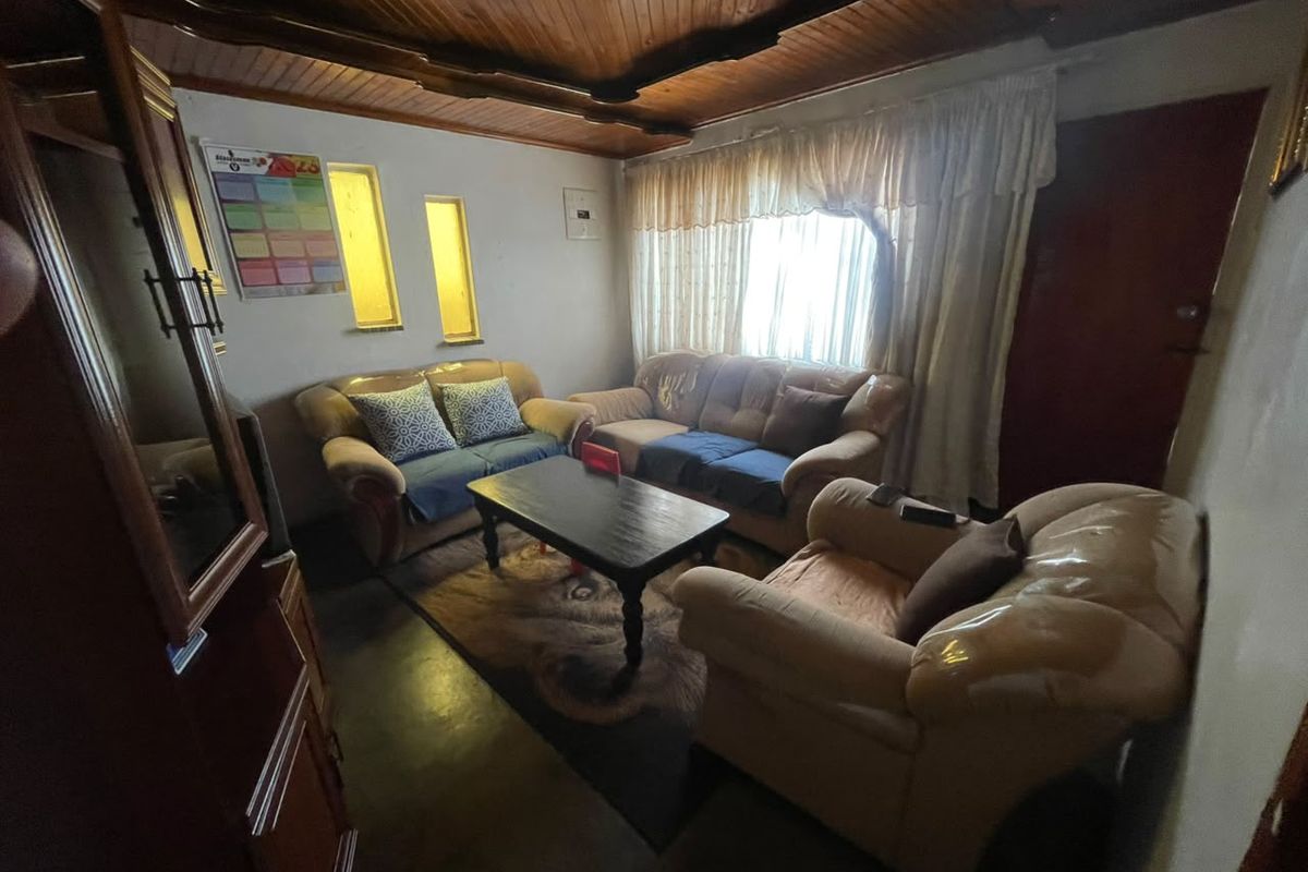 A living room featuring a timber tongue and groove ceiling and vertical slit windows, offering a dated aesthetic ready for modernization.