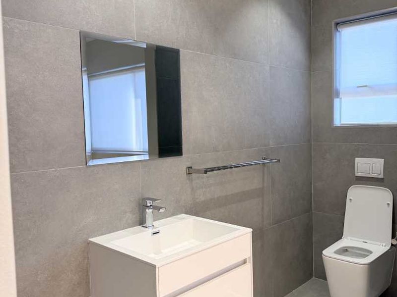 Modern bathroom featuring large format grey tiling, a sleek wall-mounted vanity with basin, and a contemporary wall-hung toilet.