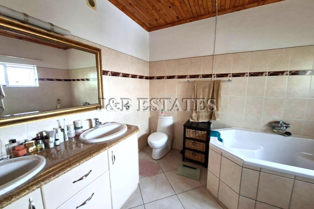 A functional bathroom featuring a double vanity with granite countertop, a corner bathtub, and a toilet, finished with neutral wall tiles.