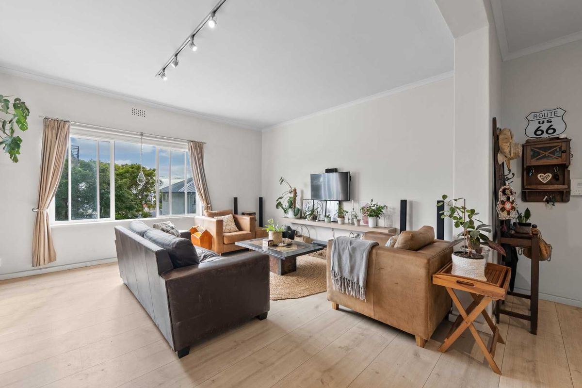 A bright and spacious living room featuring light-toned timber flooring, large windows, and modern track lighting.