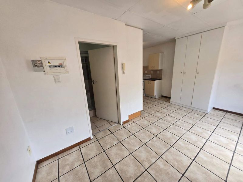 Open plan living area featuring tiled flooring, built-in storage cupboards, and a compact kitchen area with basic cabinetry.