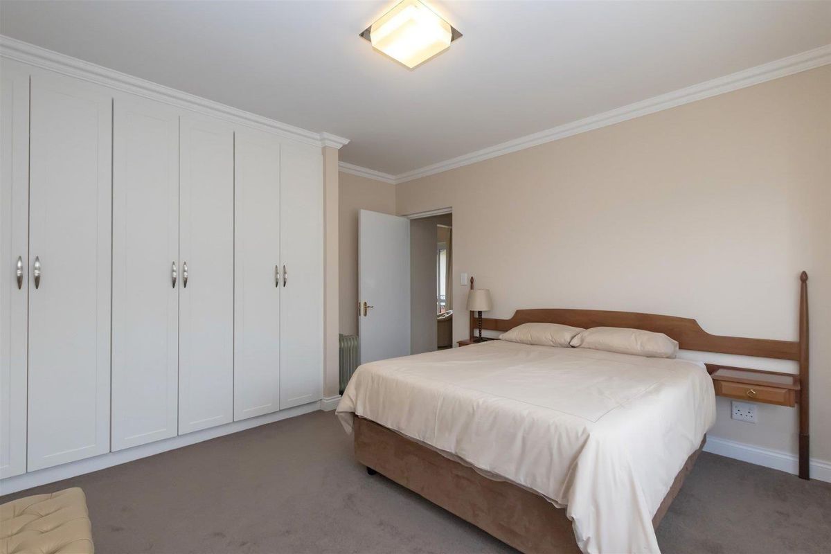 A well-maintained bedroom featuring neutral carpeting, crown molding, and extensive built-in floor-to-ceiling white cabinetry for ample storage.