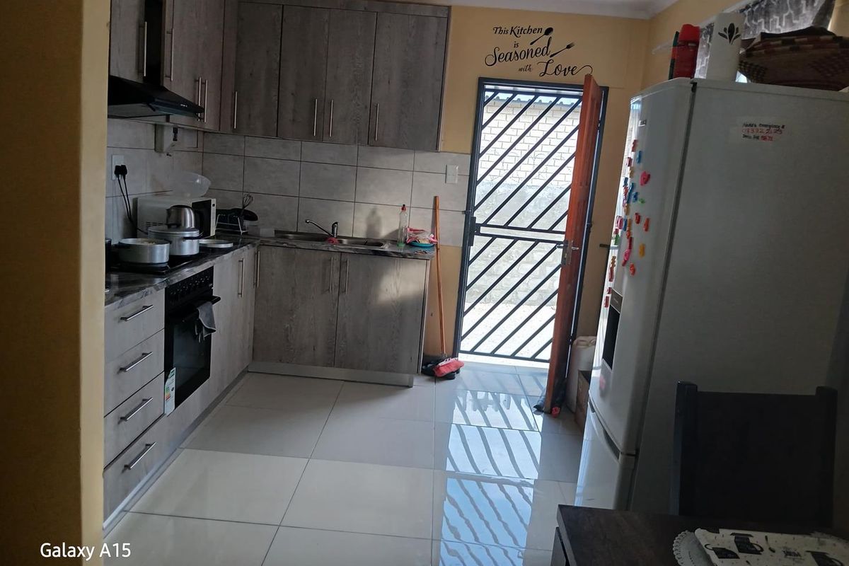 A functional kitchen featuring wood-look cabinetry, tiled flooring, a built-in oven and hob, and a security gate leading to the exterior.